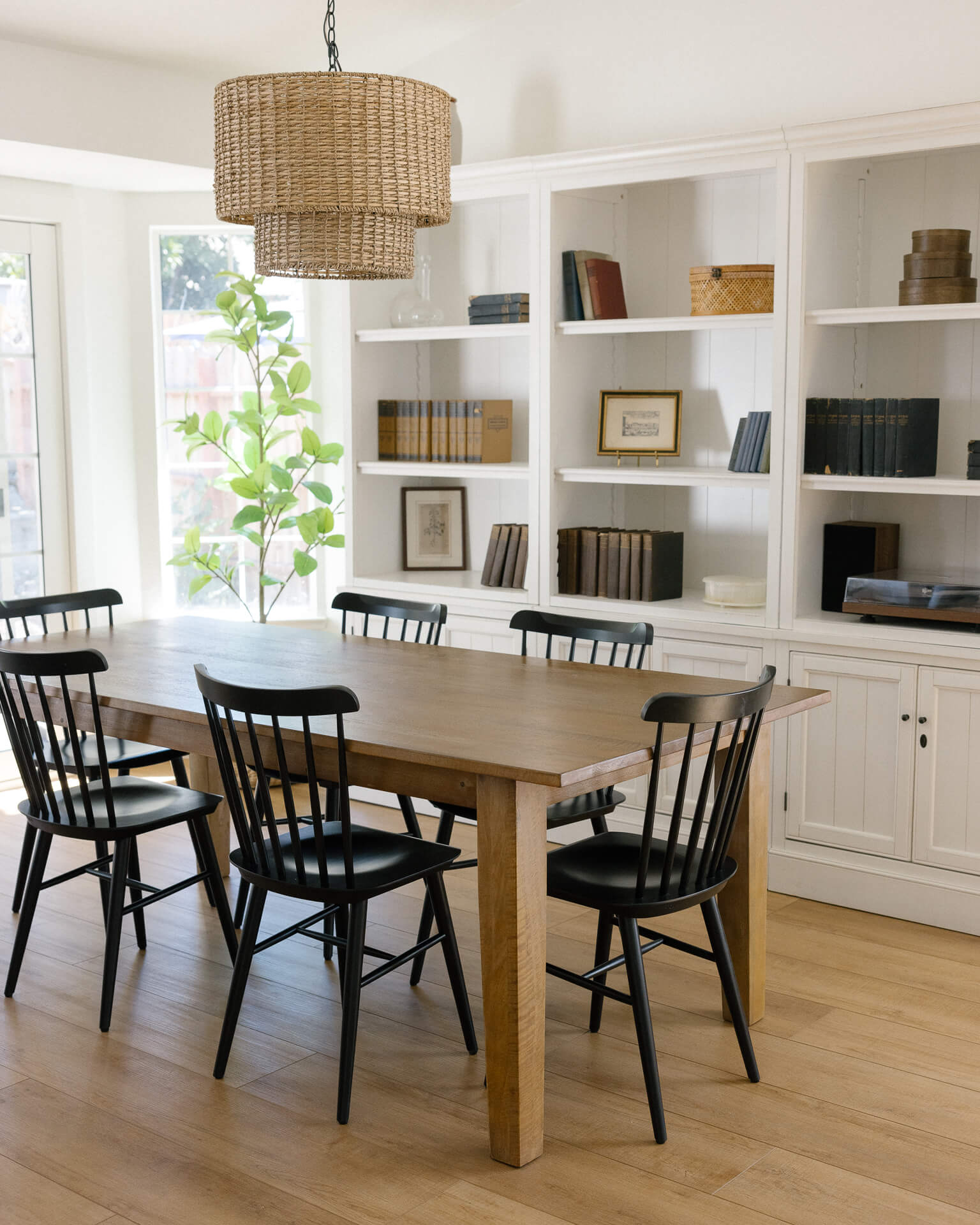 A timeless dining room styled with a white bookshelf, black chairs, Crate and Barrel dining table, and wicker chandelier