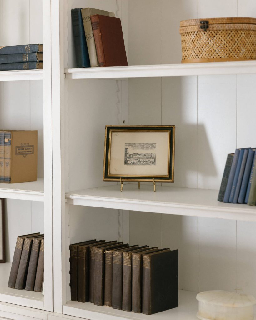 A white bookshelf styled with art and vintage books